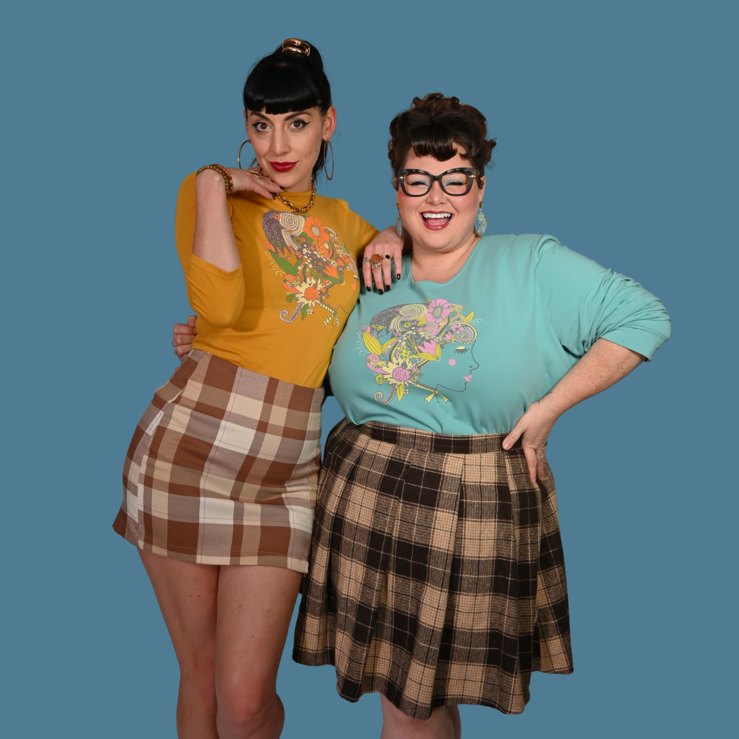 Two women posing together wearing vintage-style clothing against a blue background