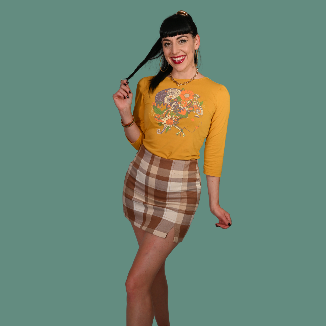 Woman wearing a yellow graphic 3/4 sleeve tee and a plaid skirt on a green background