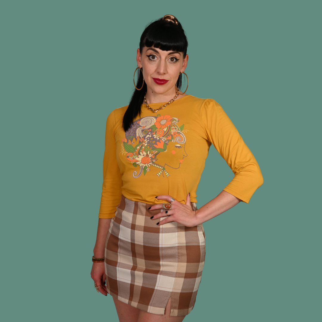 Woman wearing a mustard yellow long-sleeve top with a graphic design and a plaid skirt on a transparent background