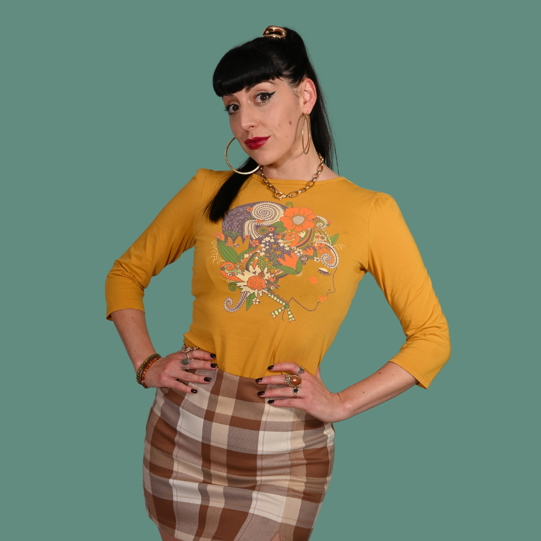Woman wearing a mustard yellow shirt with a colorful design and plaid skirt on a green background