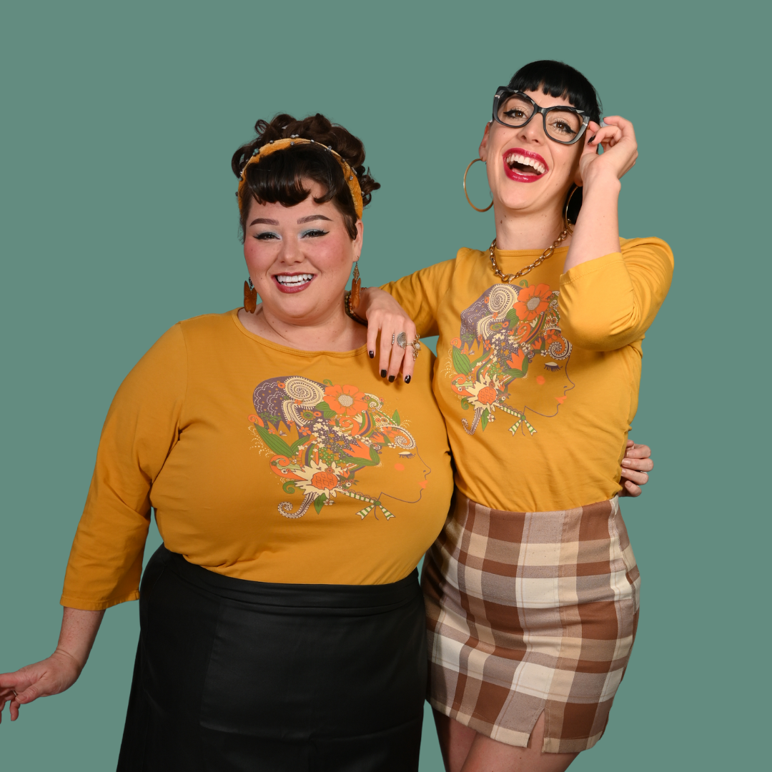 Two women wearing yellow shirts with graphic designs on a green background