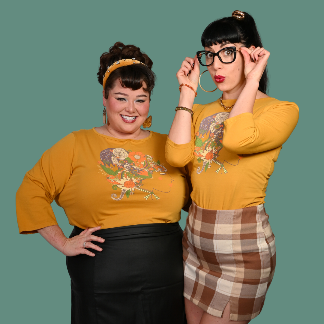 Two women wearing matching yellow tops with a design, standing against a green background.