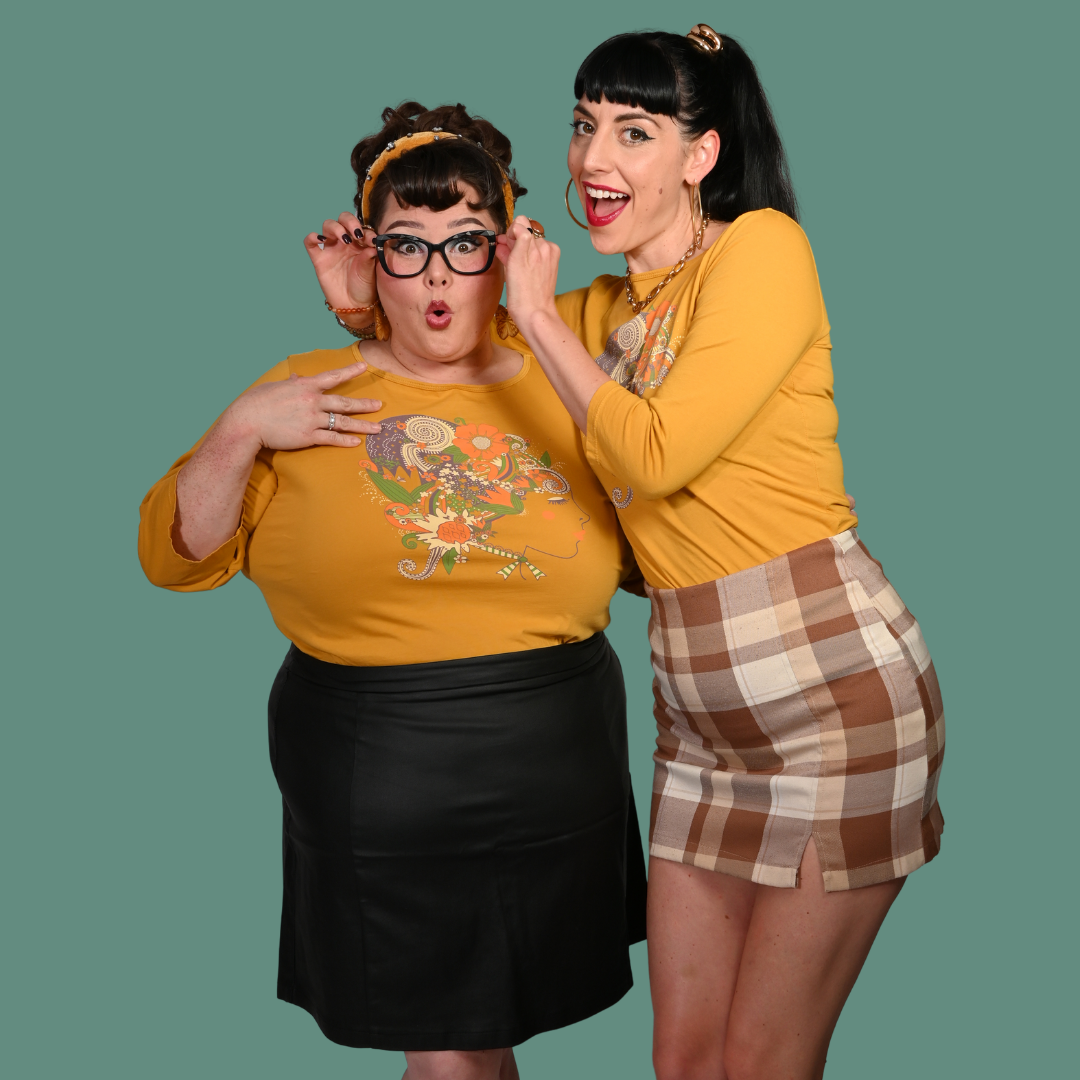 Two women in yellow graphic t-shirts and skirts posing against a green background