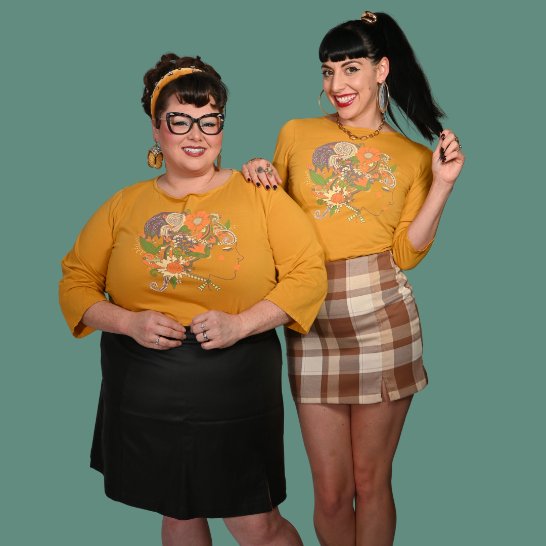 Two women wearing matching yellow graphic tees with a colorful design on a green background