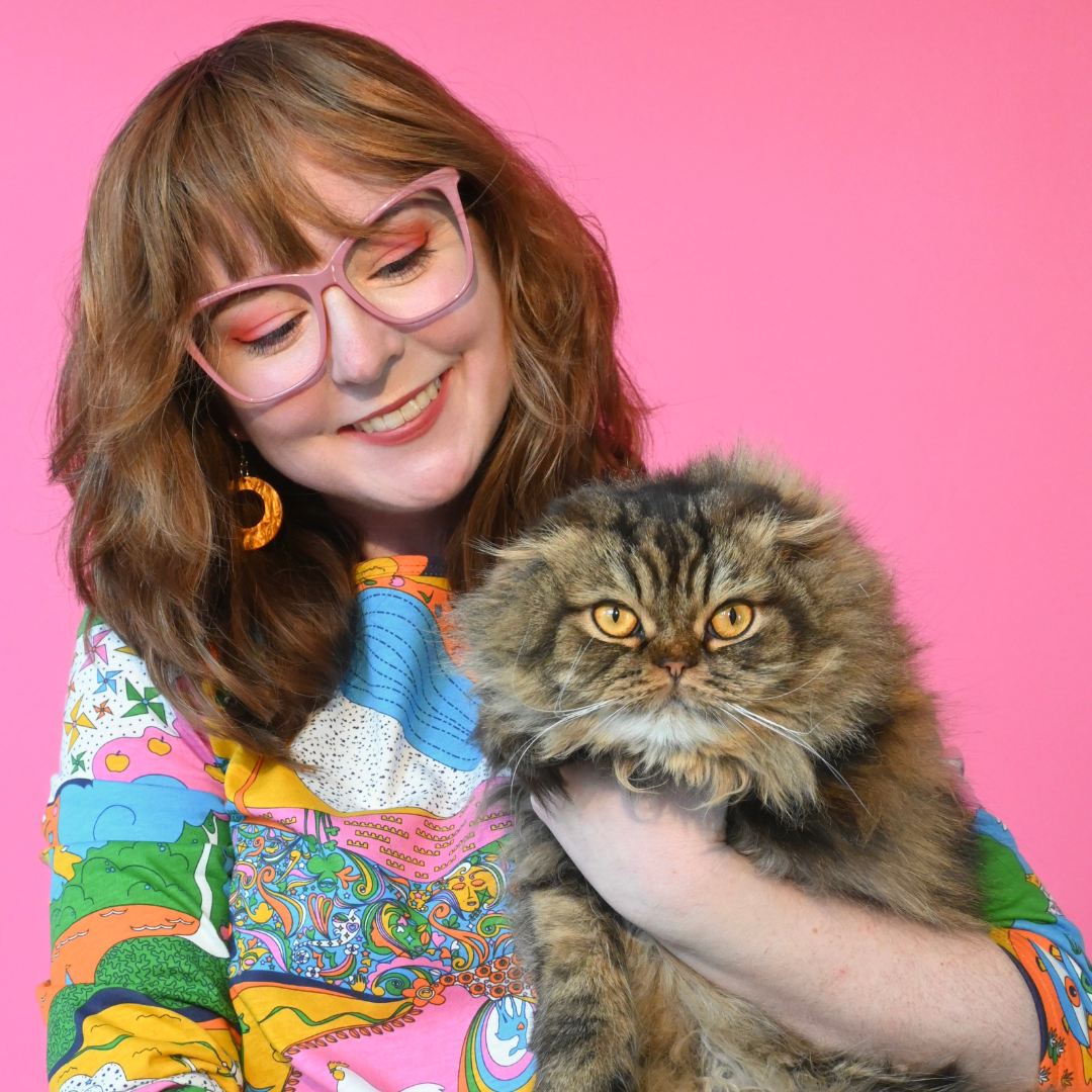 Closeup of brown-haired girl wearing glasses and our landscape print tee, and holding a cat