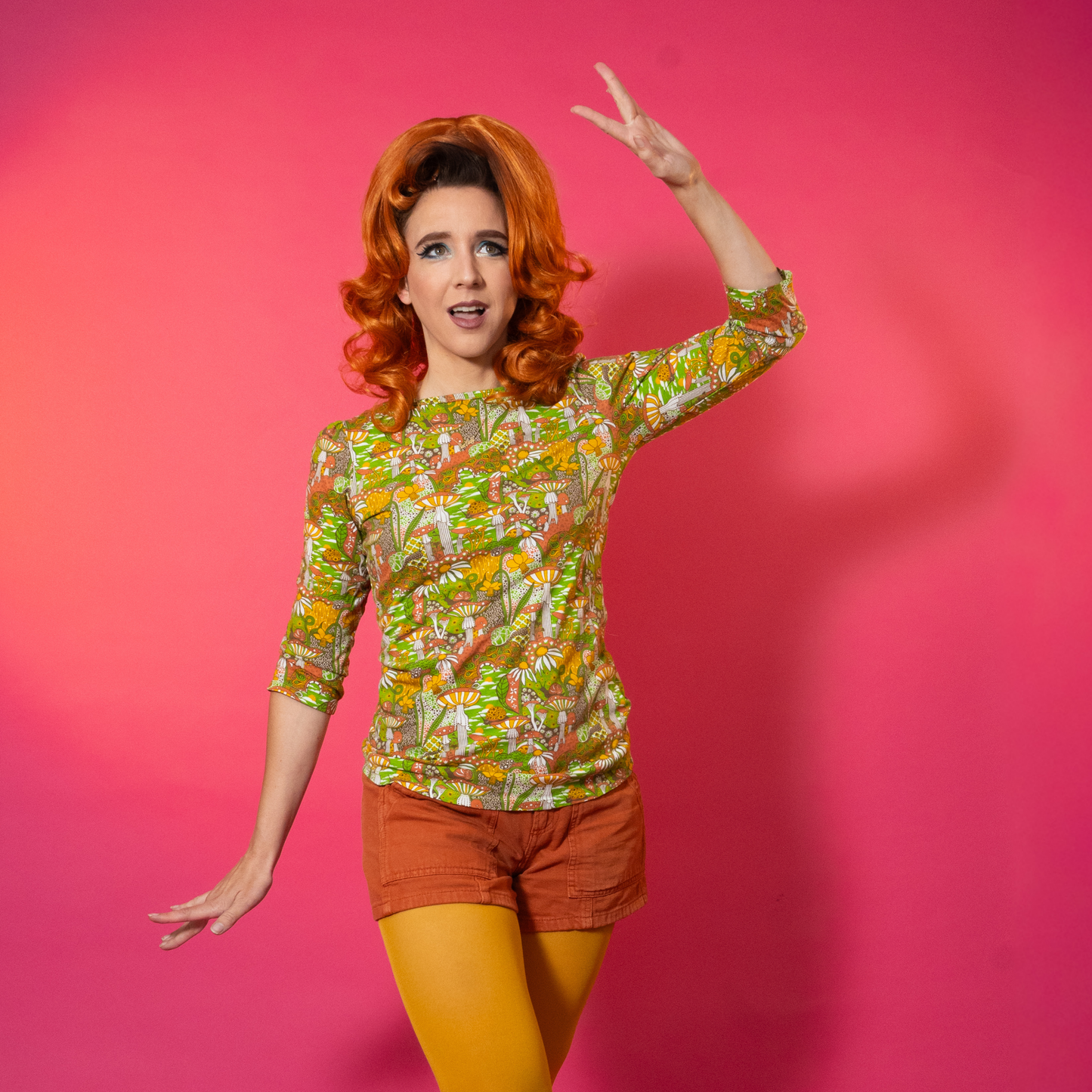Woman with red hair and a colorful patterned shirt on a pink background