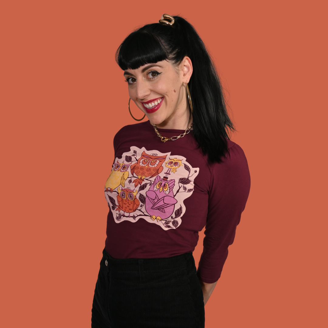 Woman wearing a reddish purple 3/4-sleeve shirt with a colorful owl design on an orange background