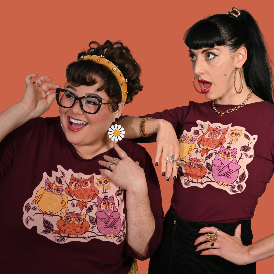 Two women wearing burgundy t-shirts with owl designs against an orange background