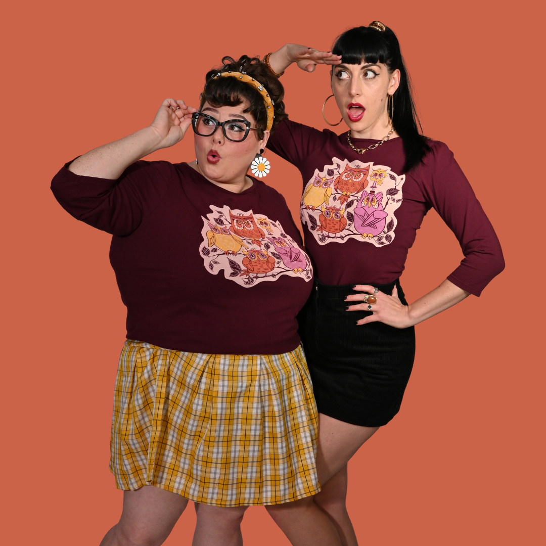 Two women wearing reddish purple graphic tees with owl designs on an orange background