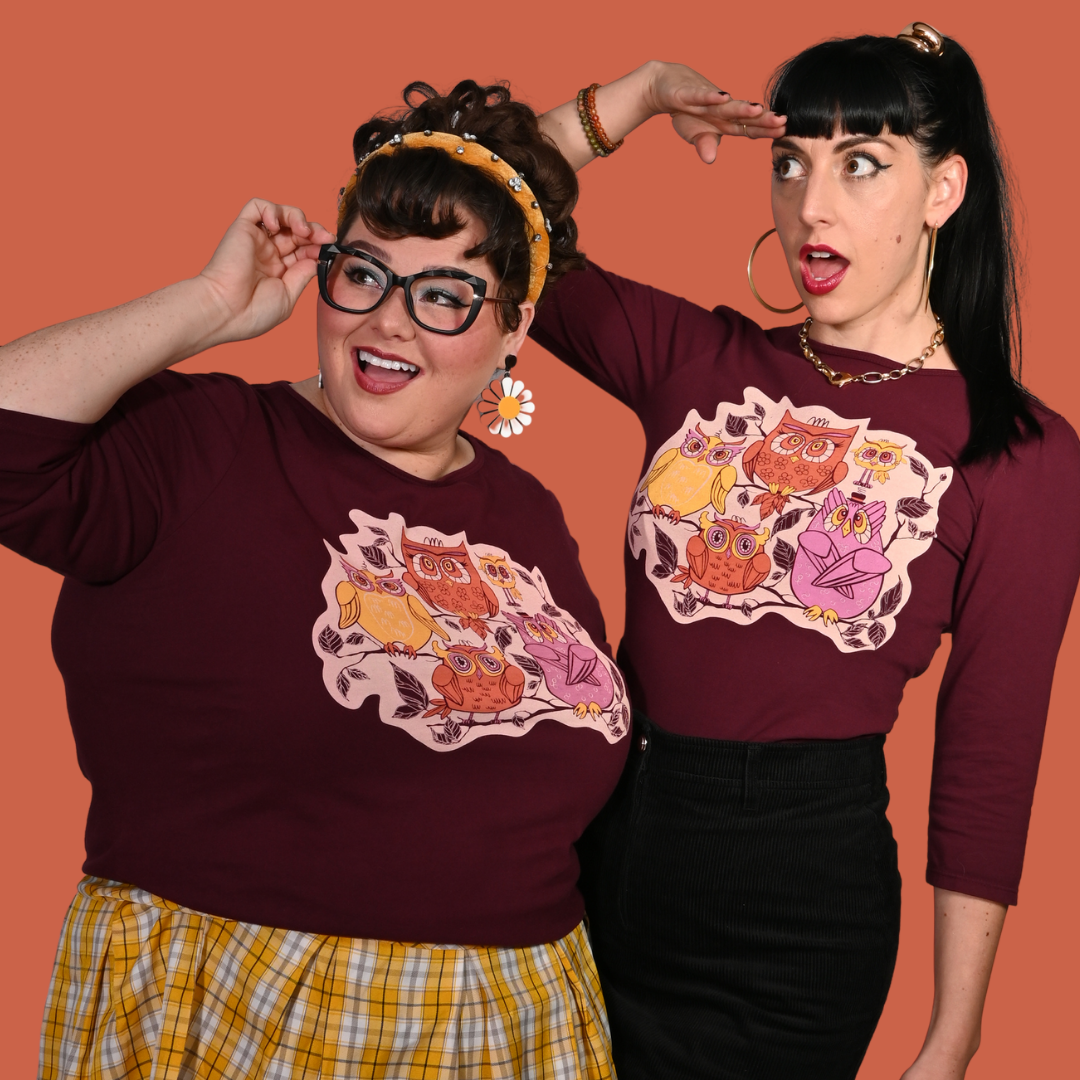 Two women wearing plum purple  shirts with owl designs against an orange background