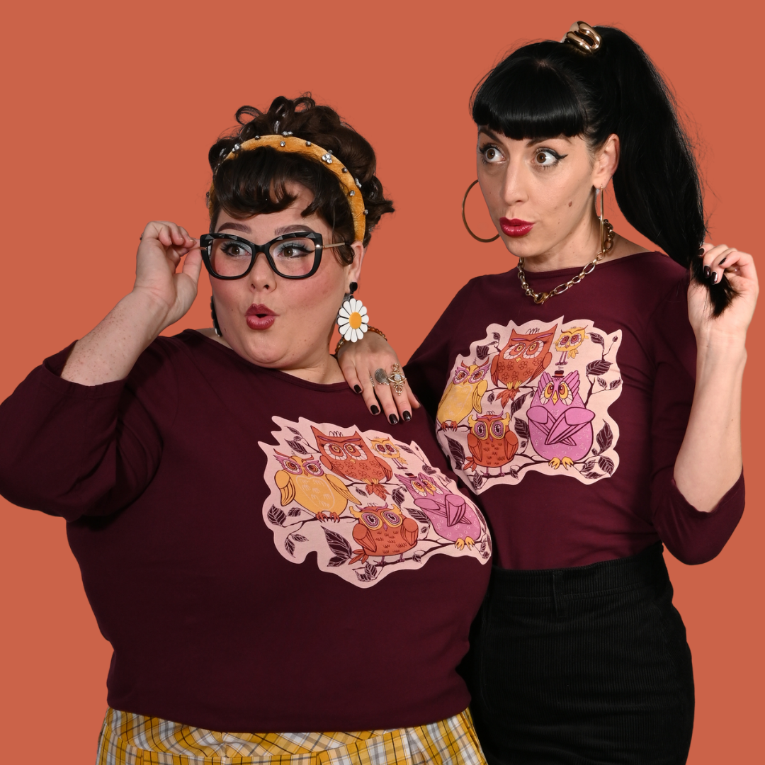 Two women wearing plum purple graphic tees with owl designs on an orange background