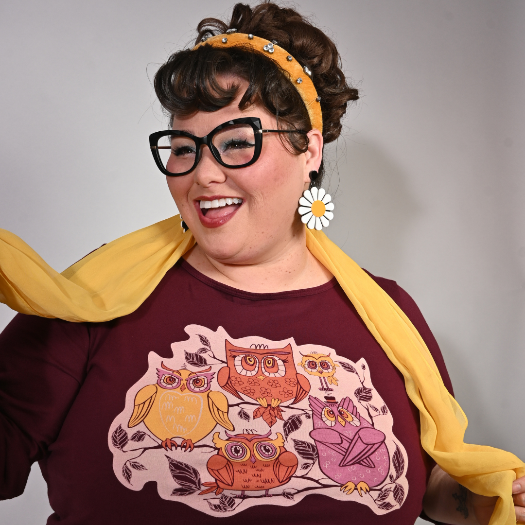 Person wearing a plum purple shirt with owl design and yellow scarf, against a plain background