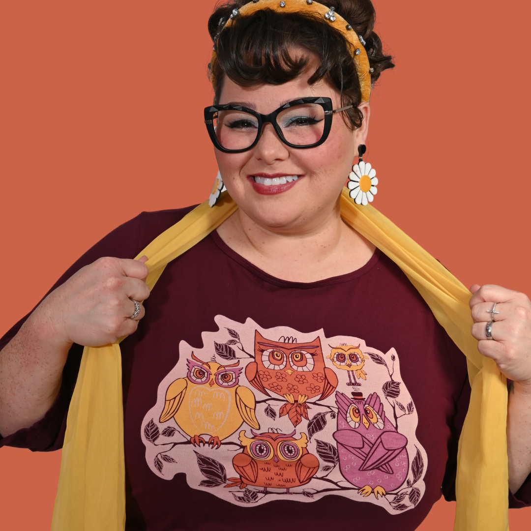 Woman wearing a plum t-shirt with owl design and a yellow scarf against an orange background