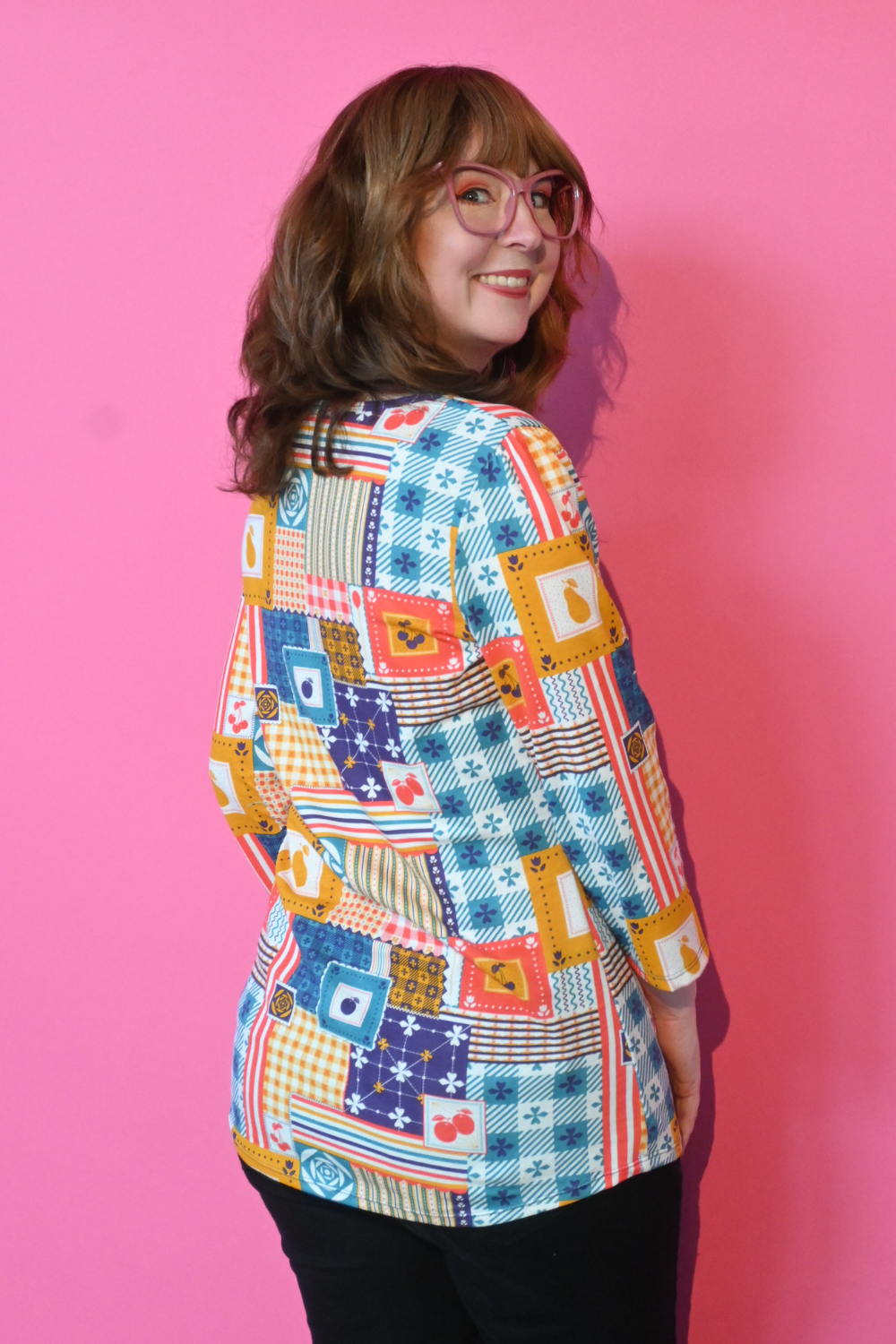 Back view of redhead model in glasses wearing 3/4 sleeve tee featuring colorful patchwork