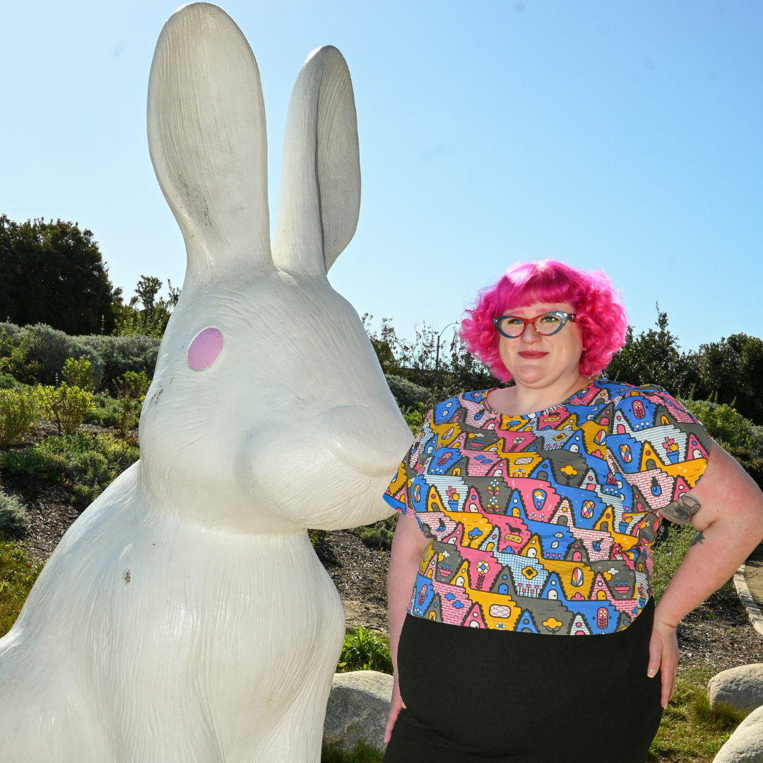 Cute pink-haired model with glasses n geometric print tee, standing near huge bunny statue