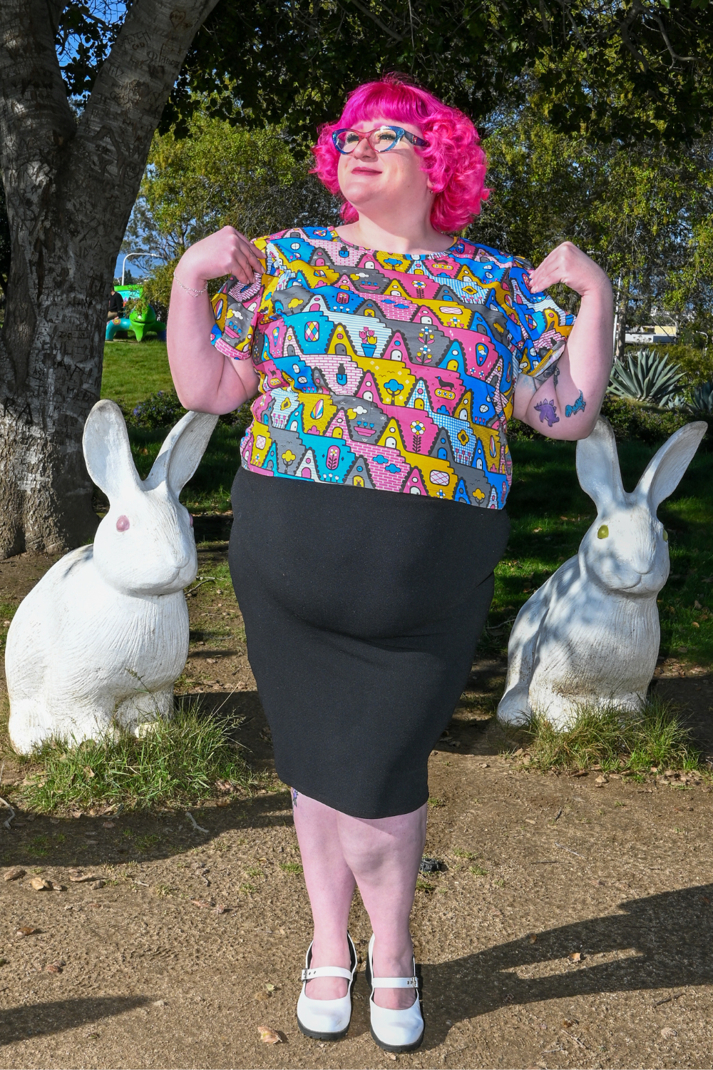 Pink-haired model wearing geometric print tee in cute pose with bunny statues behind her