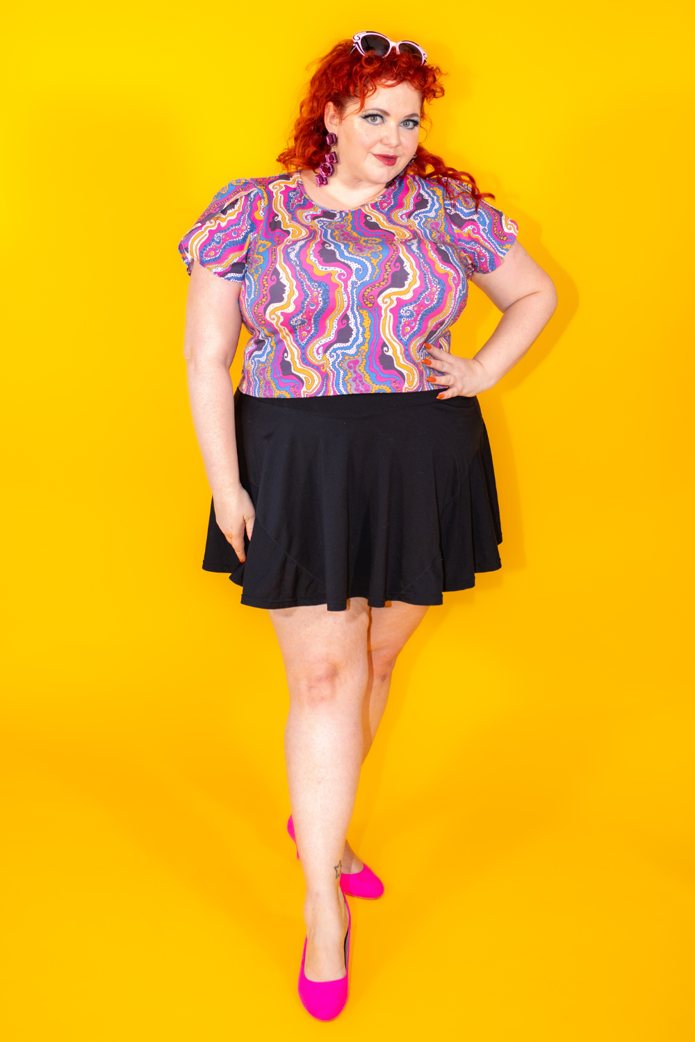 Red haired model in psychedelic print shirt with black miniskirt and pink shoes