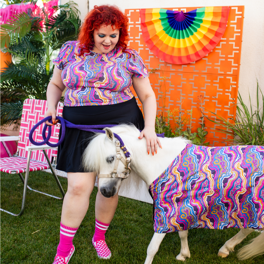 Red-haired model in sychedelic tee with white mini horse in matching purple print clothing