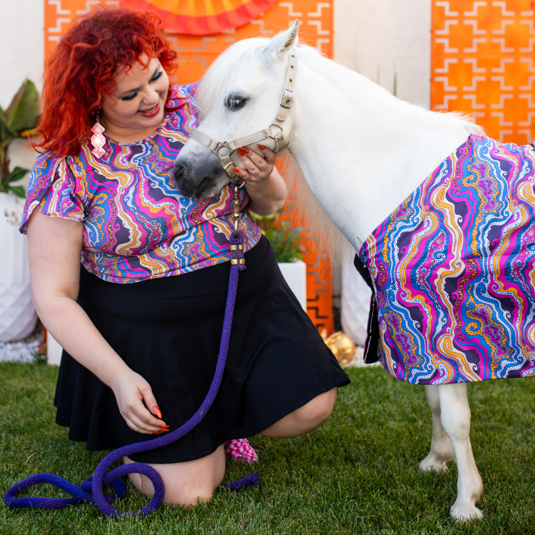 Red haired model and white mini horse in psychedelic print clothing