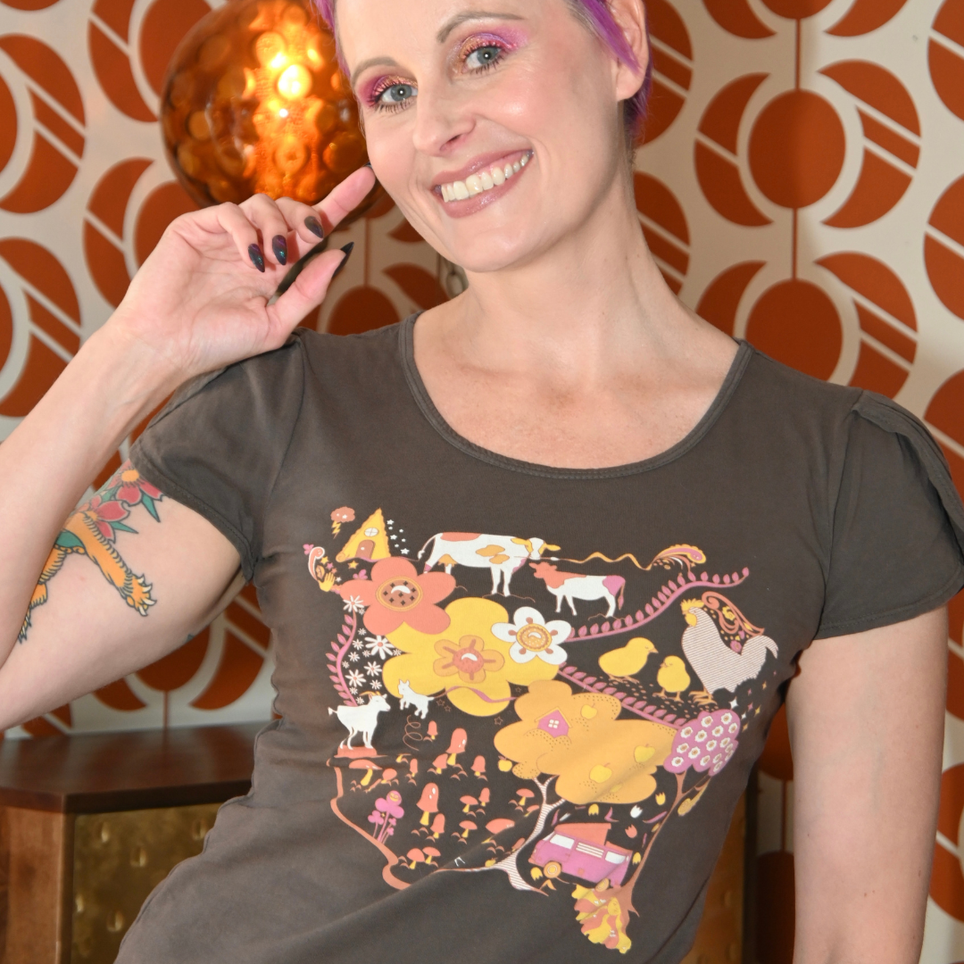 Pink-haired model in brown graphic tee with landscape print