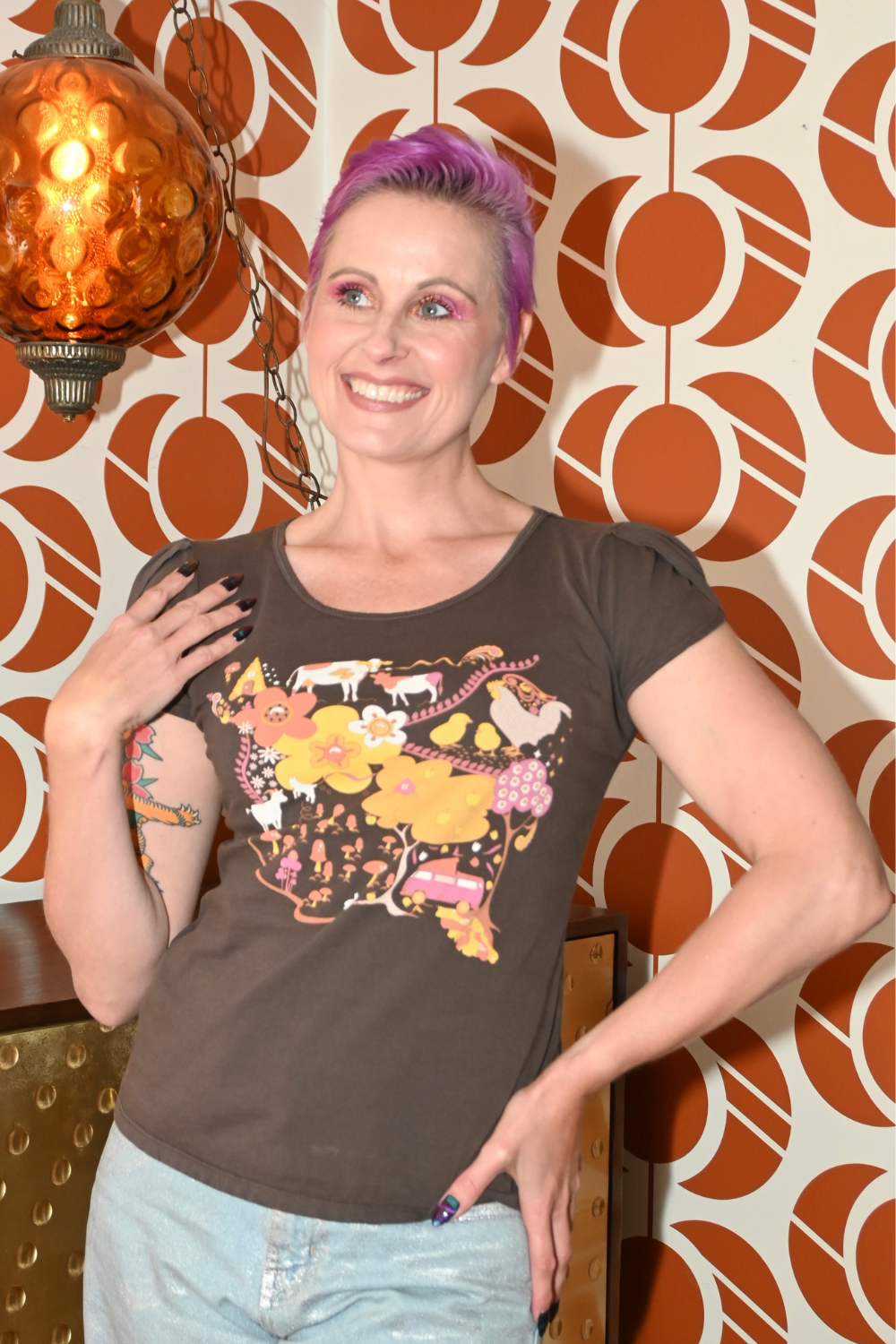 Pink-haired model in brown graphic tee with landscape print