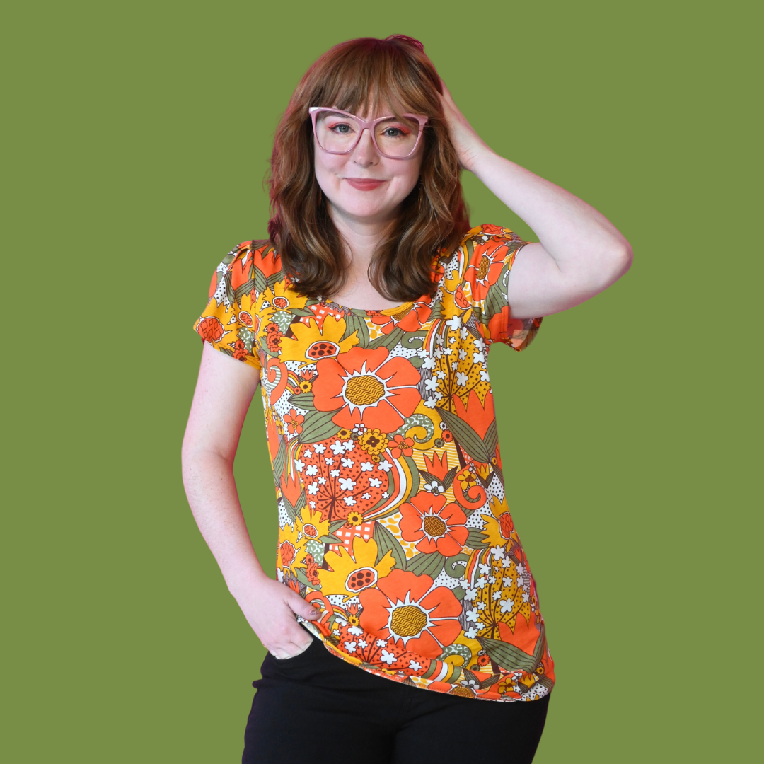 Girl in glasses wearing bright colored tee with large floral print on green background