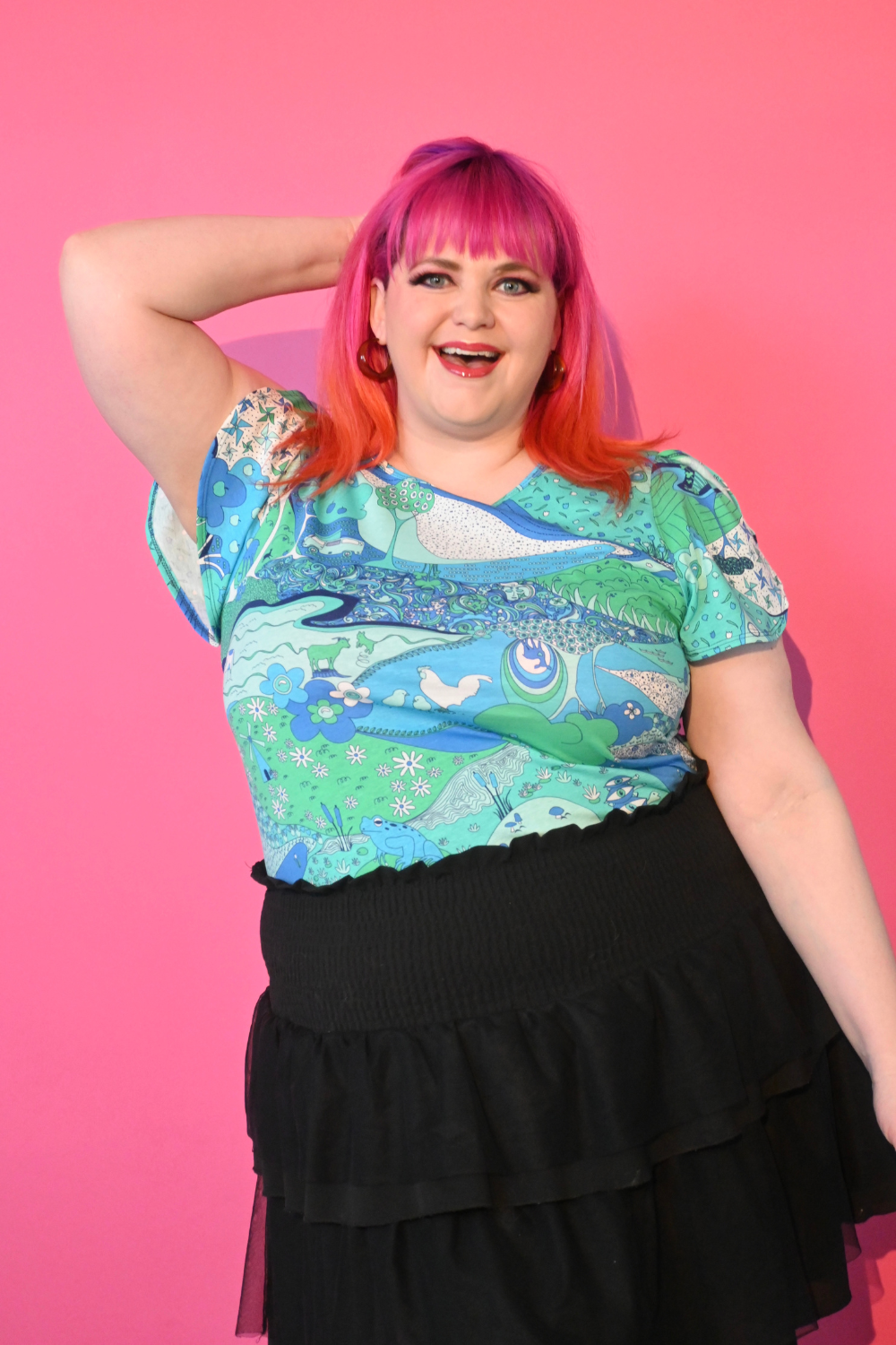 Pink haired model wearing shirt with landscape graphic in green and blue