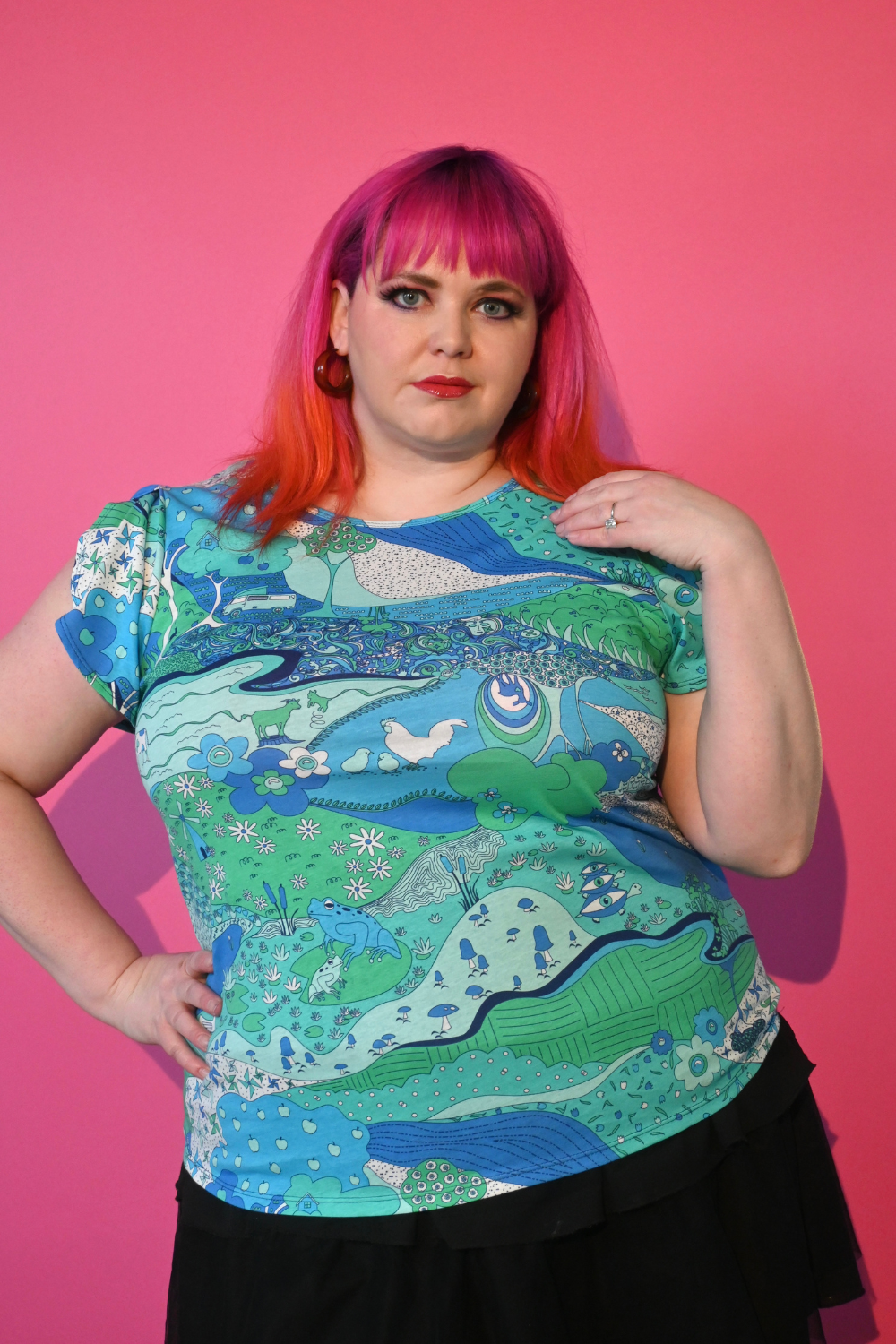 Pink haired model wearing shirt with landscape graphic in green and blue