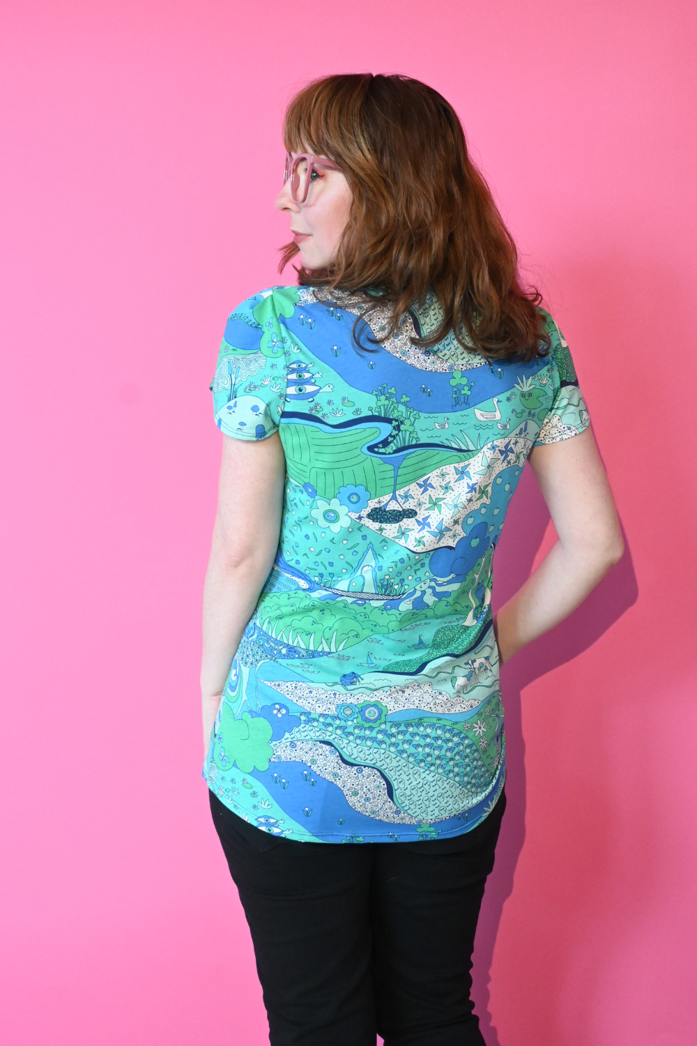 Back view of model wearing shirt with landscape graphic in green and blue