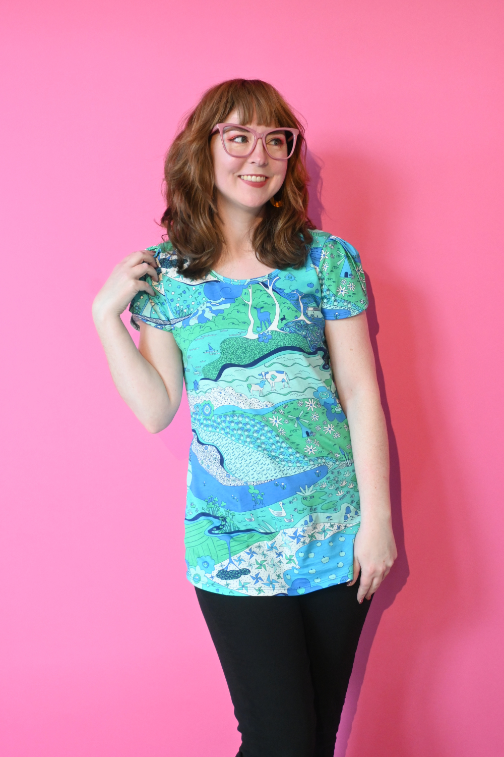 Model with glasses wearing shirt with landscape graphic in green and blue