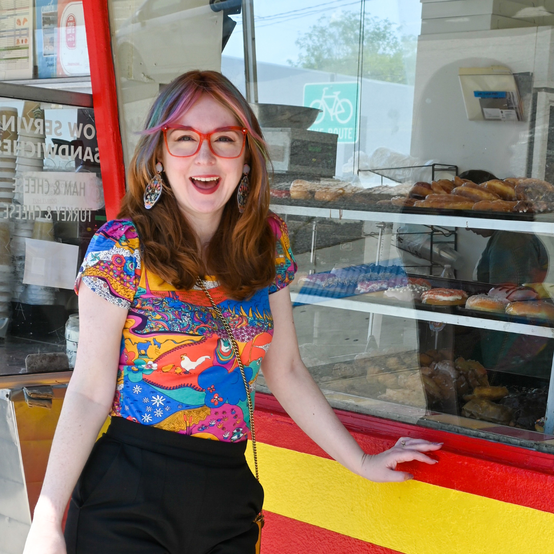 Cute model wearing colorful shirt and smiling in front of donut counter