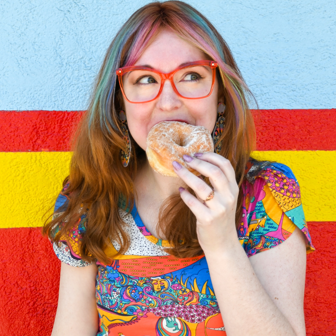 Cute model with fun hair eating a donut and wearing bright glasses in printed tulip sleeved tee