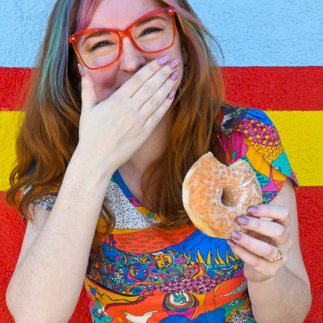 Cute model in glasses and brightly colored tee eating a doughnut