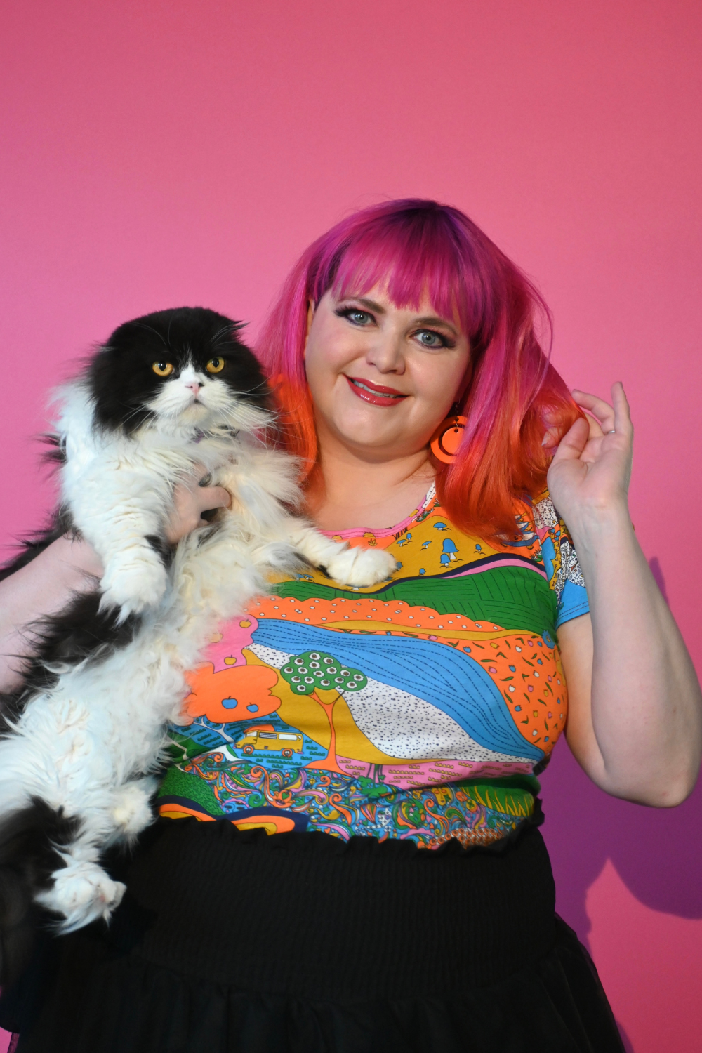 Pink haired model holding cat wearing shirt with landscape graphic in multicolor
