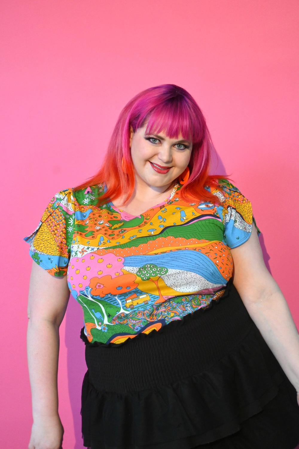 Pink haired model wearing shirt with landscape graphic in multicolor