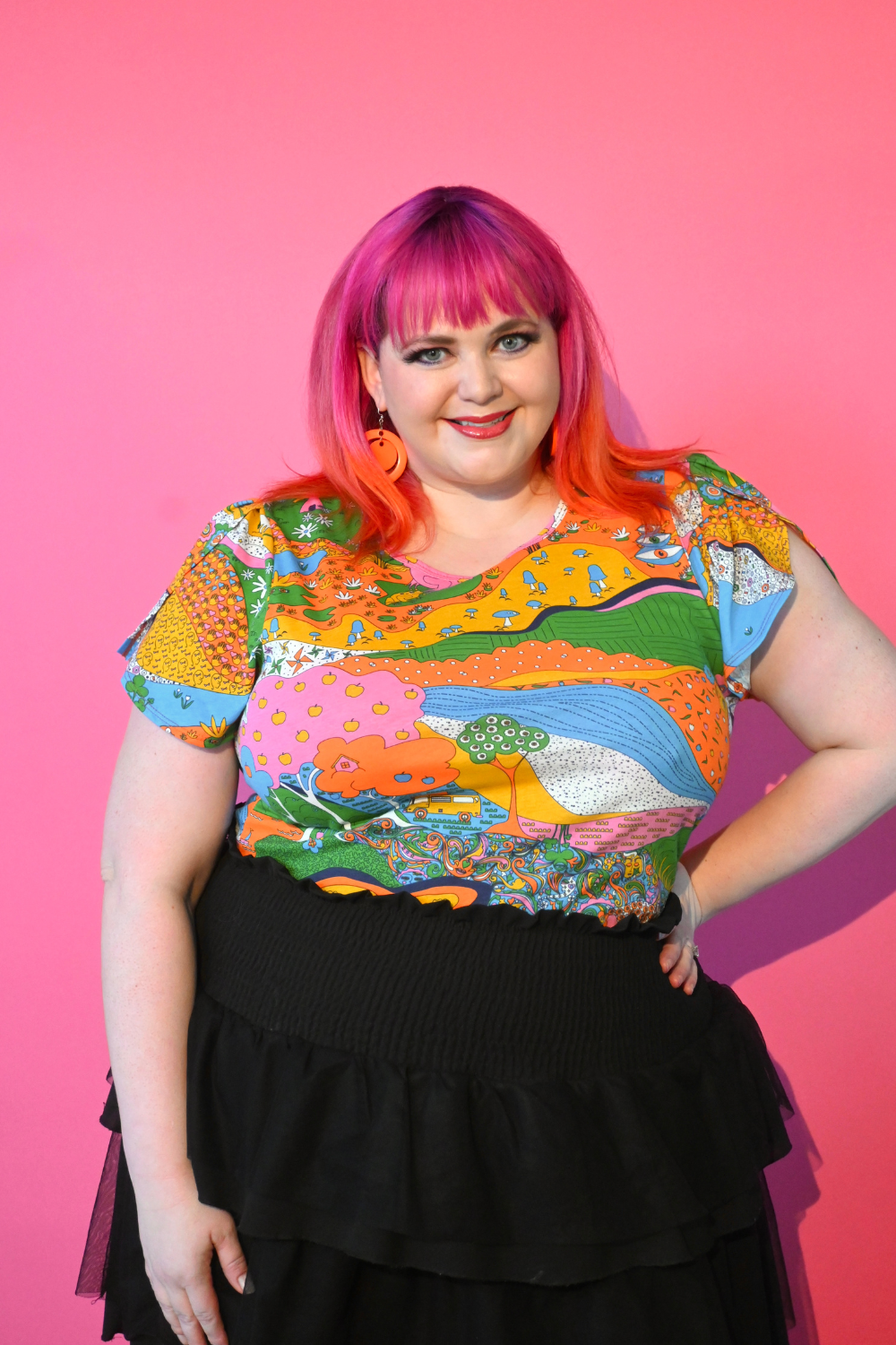 Pink haired model wearing shirt with landscape graphic in multicolor