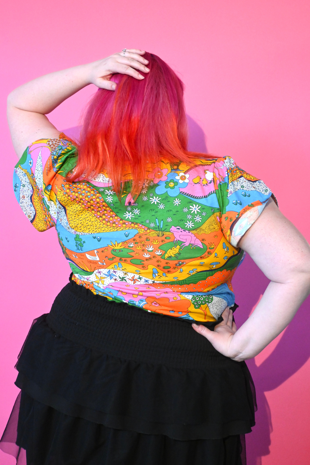 Back view of pink haired model wearing shirt with landscape graphic in multicolor