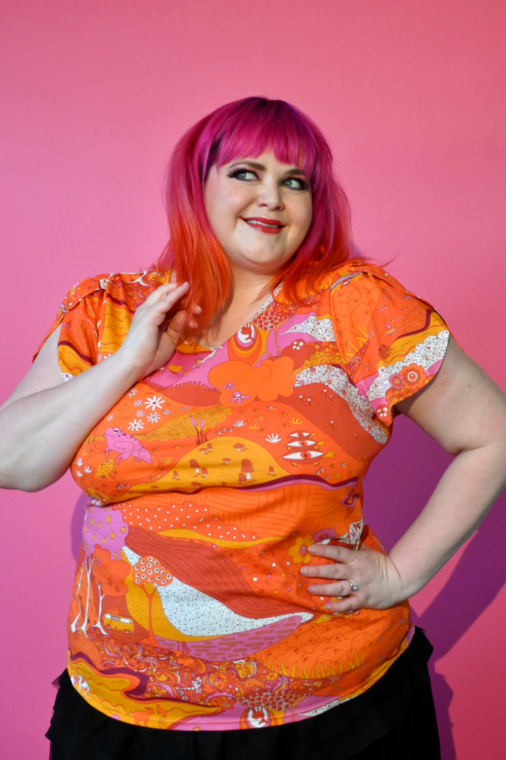Pink haired model wearing shirt with graphic of a landscape in orange and pink