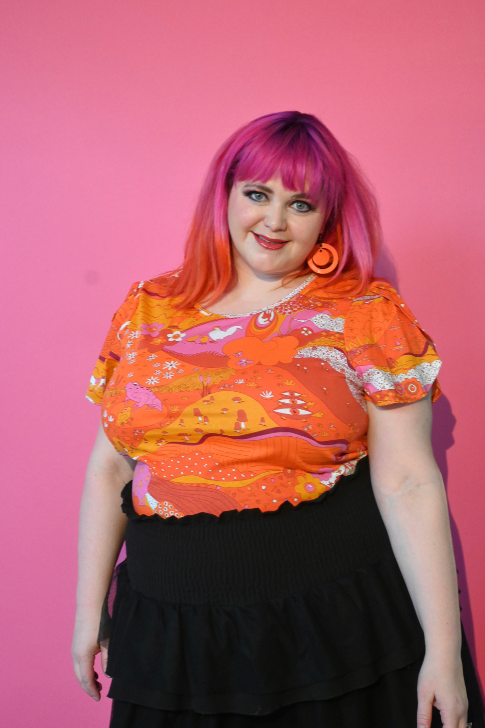 Pink haired model wearing shirt with graphic of a landscape in orange and pink