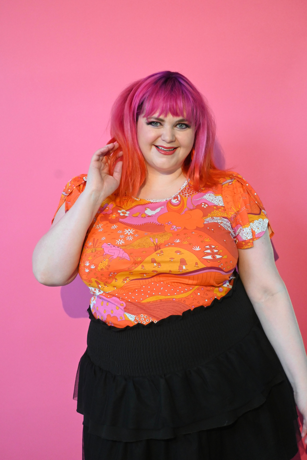 Pink haired model wearing shirt with graphic of a landscape in orange and pink