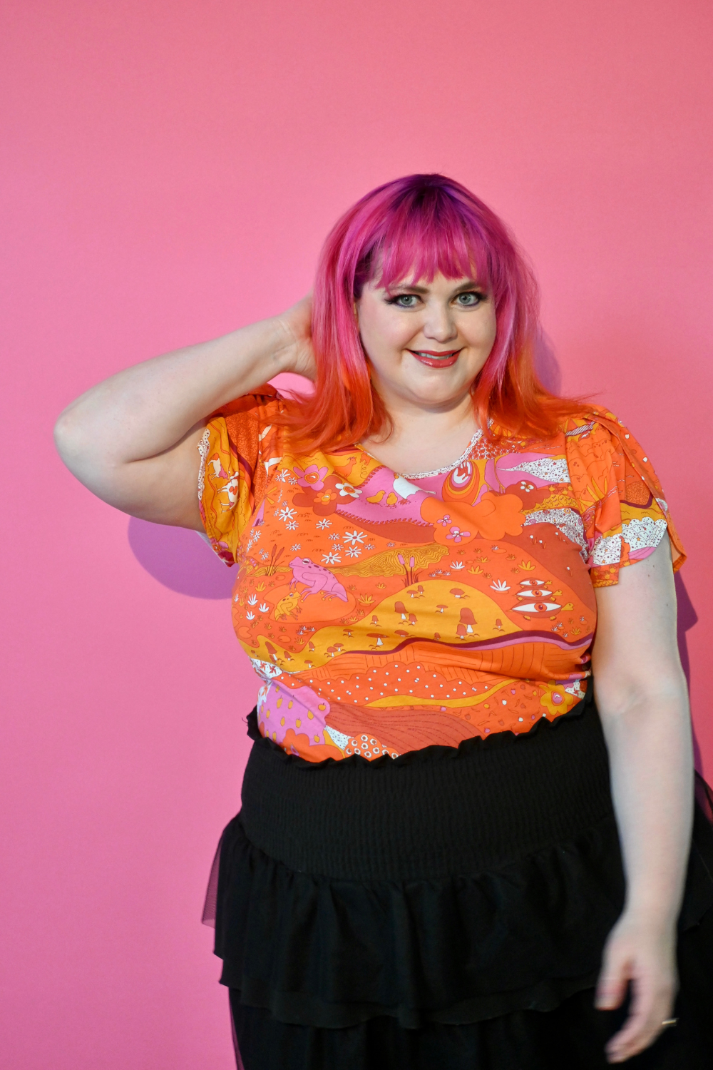 Pink haired model wearing shirt with graphic of a landscape in orange and pink