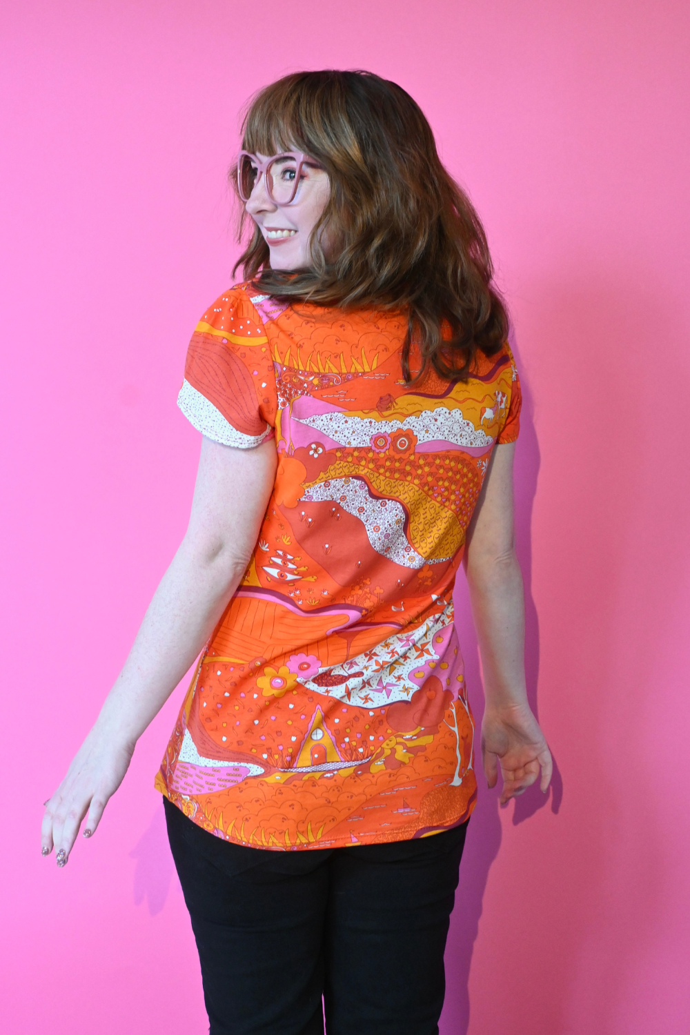 Back view of model wearing glasses and shirt with graphic of a landscape in orange and pink