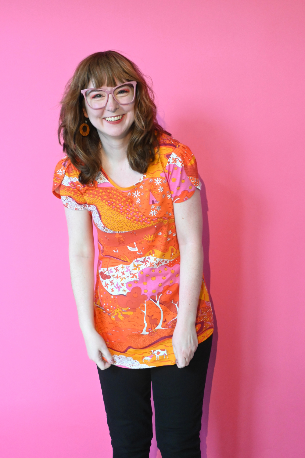 Model wearing glasses and shirt with graphic of a landscape in orange and pink