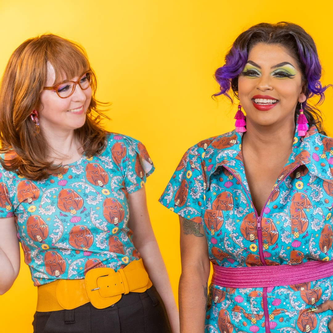 2 models  laughing, in teal tiki print clothing 