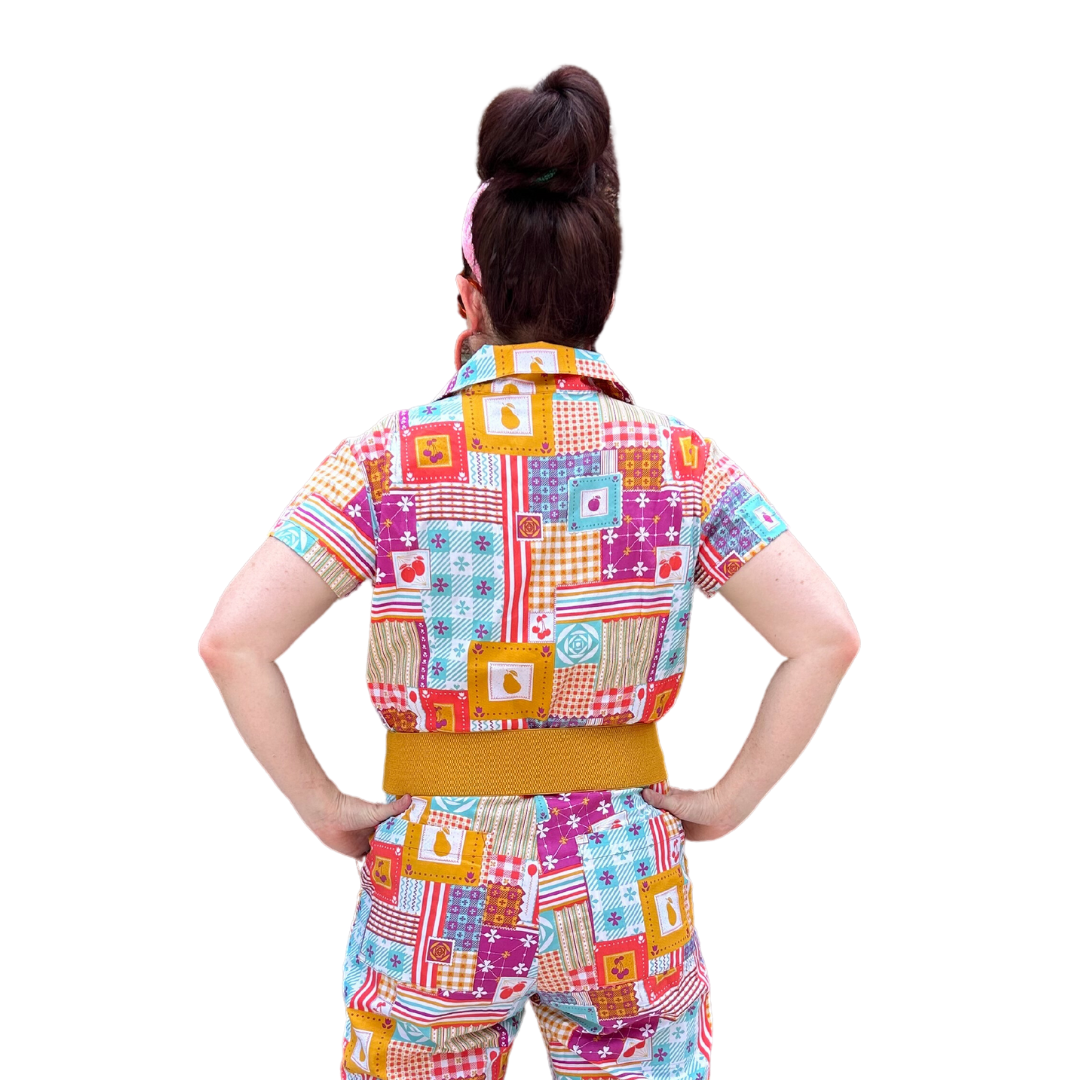 Back view of model wearing sunglasses and patchwork print zip-front collared jumpsuit with belt