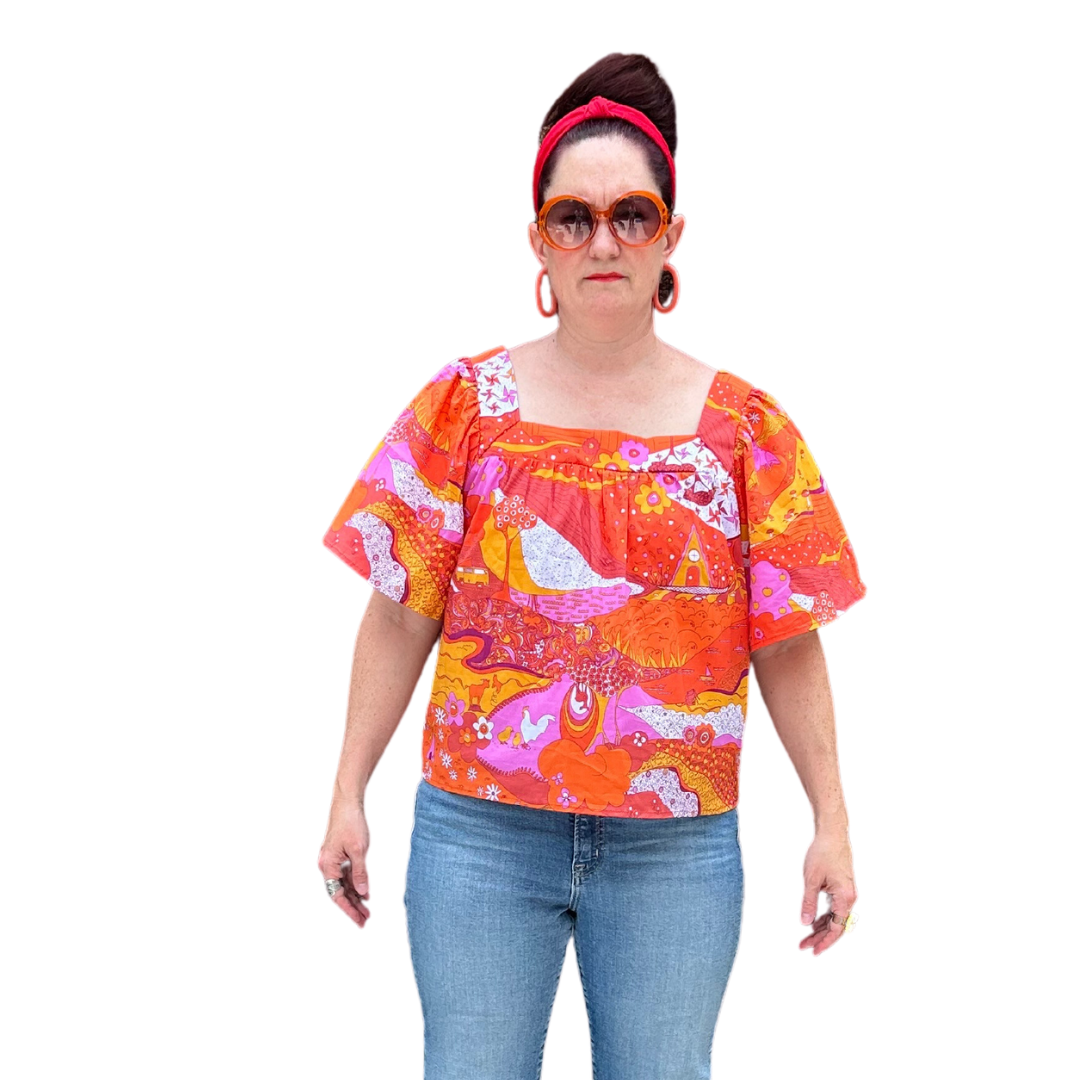Model in brightly colored woven square-neck top with landscape print in pink, orange and yellow