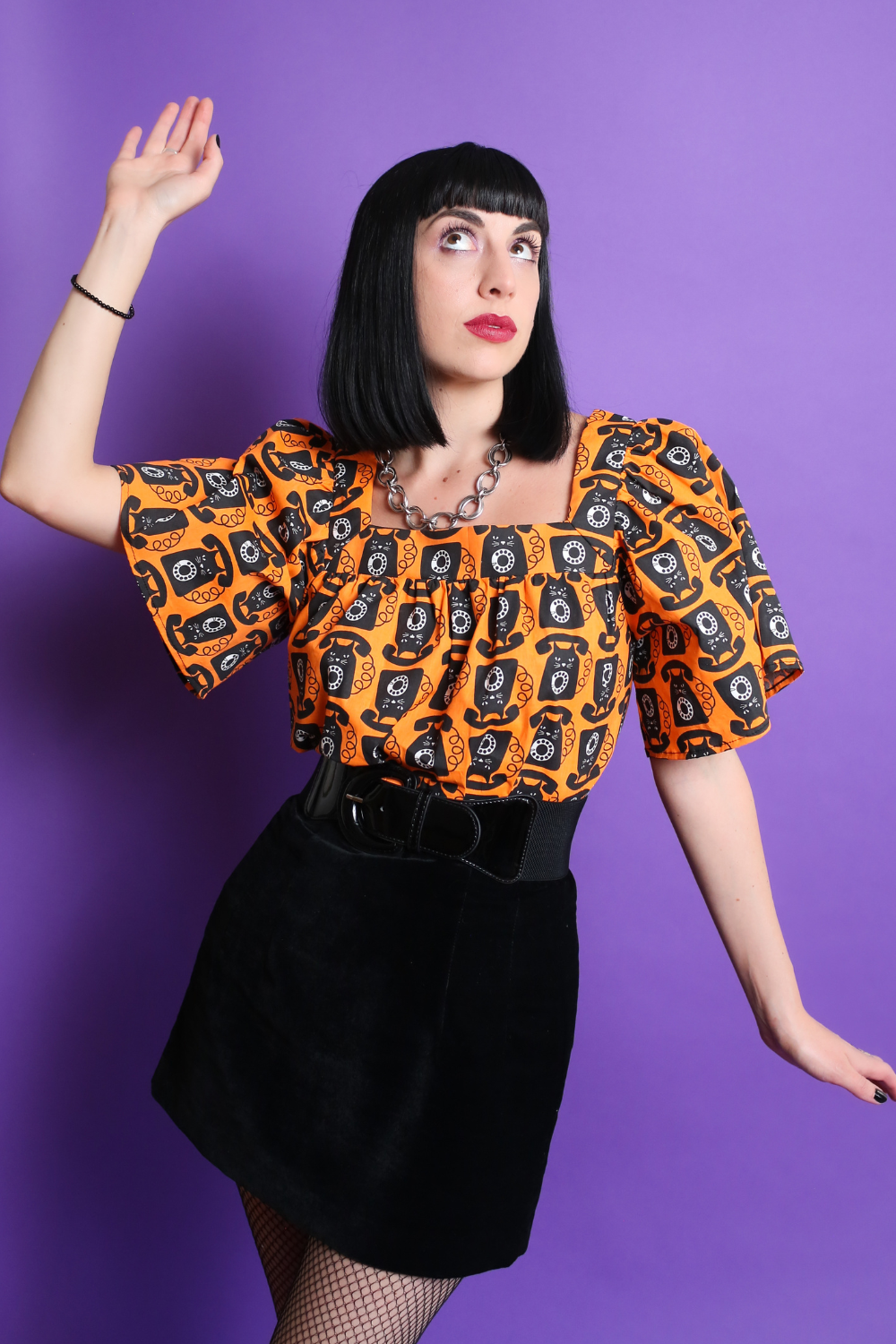 Black haired model in orange and black cat phone print top & mini skirt, posing dramatically