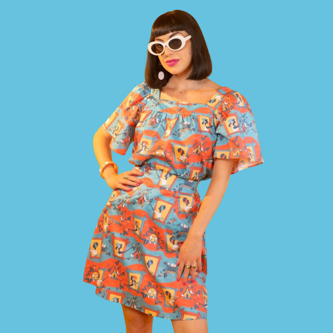 Model wearing sunglasses and red, yellow and blue print of ladies in windows and birdhouses