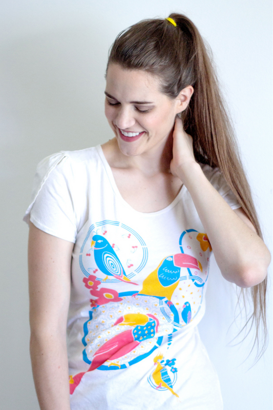 Model with long brown hair wearing graphic tee featuring tiki birds design and jean shorts