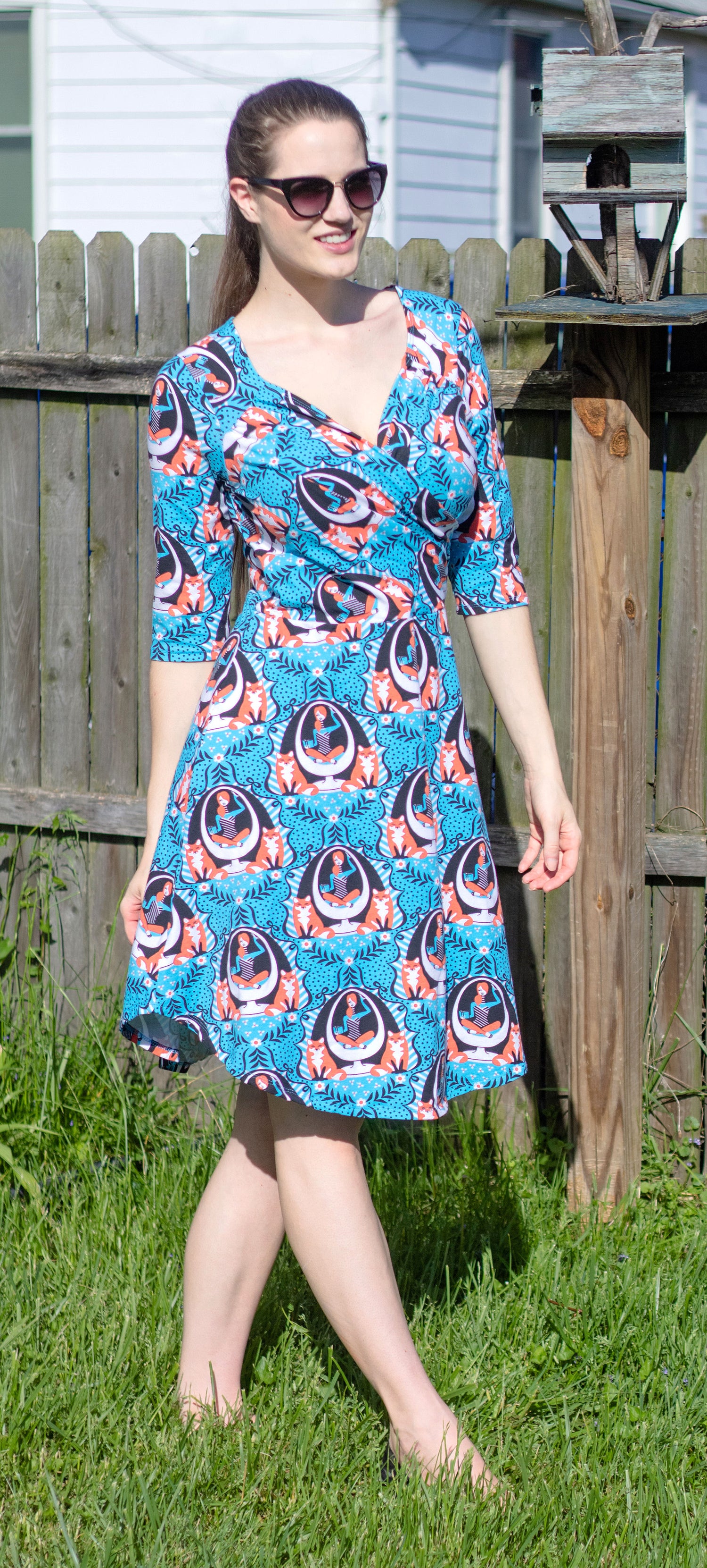 Model walking outside in blue sleeved wrap dress featuring print of foxes and girls reading books sitting in an egg chair
